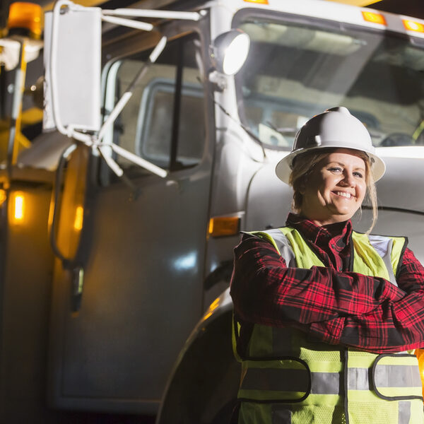 Mature woman in safety vest, hardhat with truck