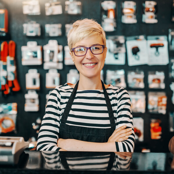 Portrait of beautiful smiling Caucasian female worker with short blonde hair standing in bicycle shop with arms crossed.