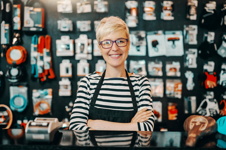 Portrait of beautiful smiling Caucasian female worker with short blonde hair standing in bicycle shop with arms crossed.
