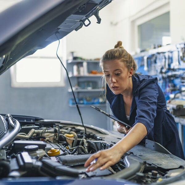 Lovely female auto mechanic, examining engine of an automobile