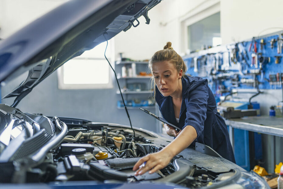 Lovely female auto mechanic, examining engine of an automobile