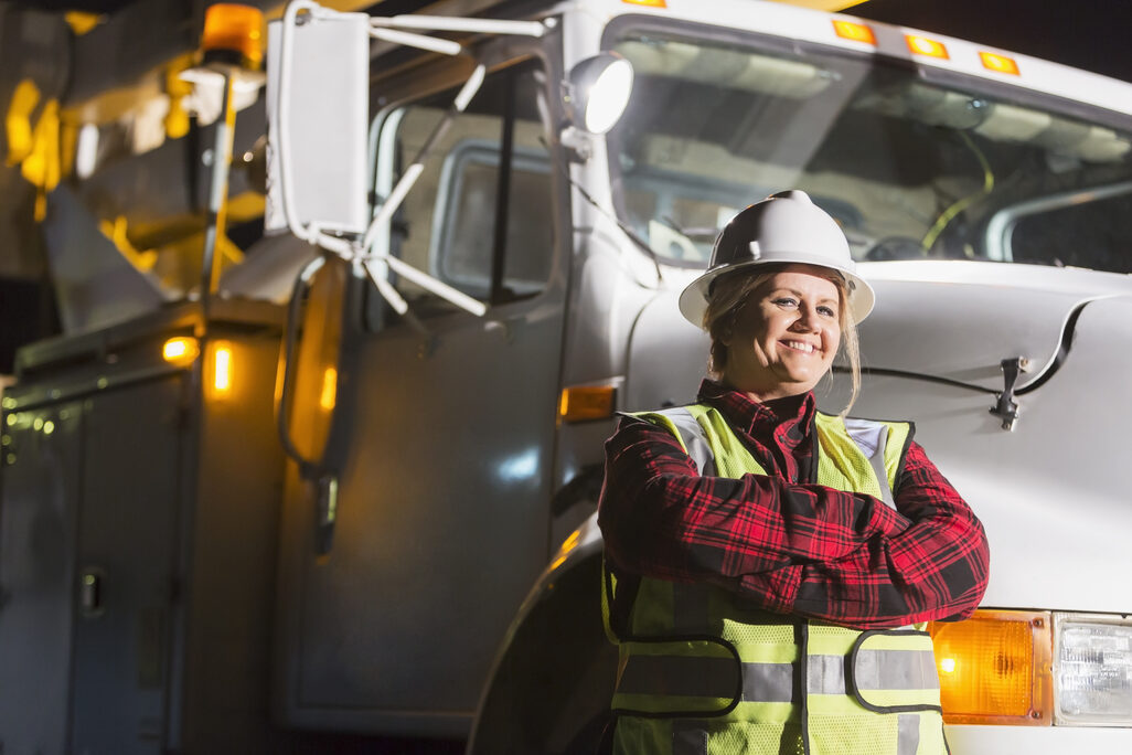 Mature woman in safety vest, hardhat with truck